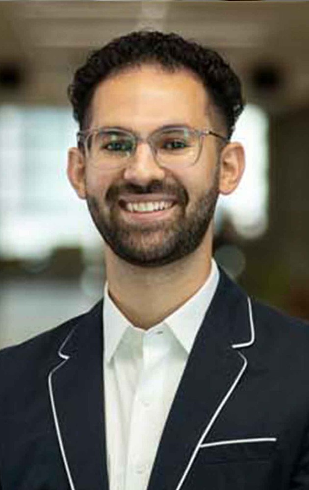 2021 Ilitch School MBA graduate, Simon Mourani, stands indoors and smiles for a headshot